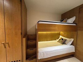 Un dormitorio pequeño con una litera, un armario de madera y cajones empotrados.