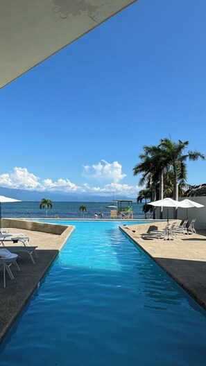 A swimming pool with lounge chairs and umbrellas, a lifeguard tower, and a view of the ocean and mountains. - Zantamar La Cruz Beach & Pool (La Cruz de Huanacaxtle)