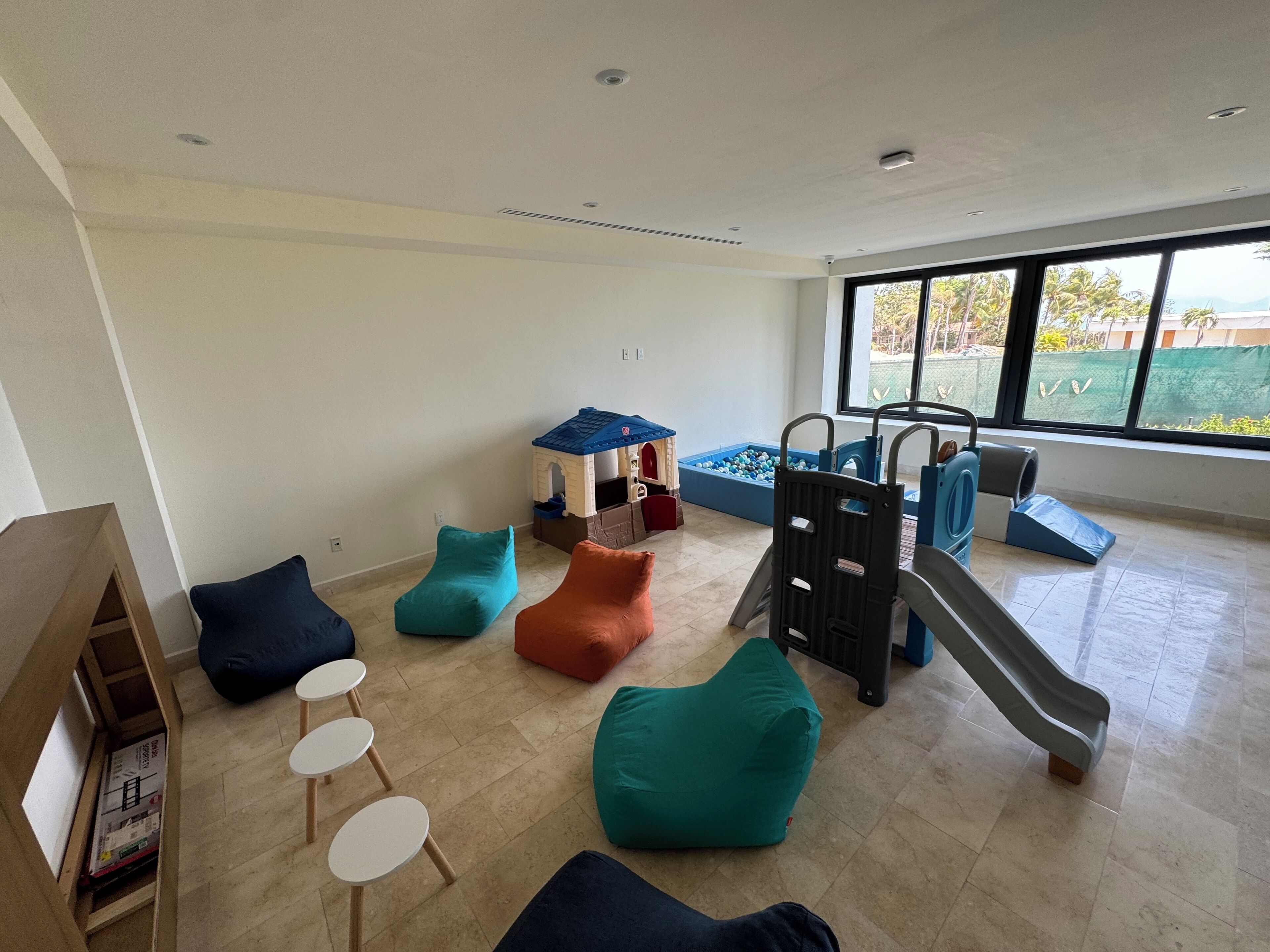 A spacious room with a play area, including a slide and a ball pit, and a large window offering a view of the outdoors.