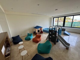 A spacious room with a play area, including a slide and a ball pit, and a large window offering a view of the outdoors.