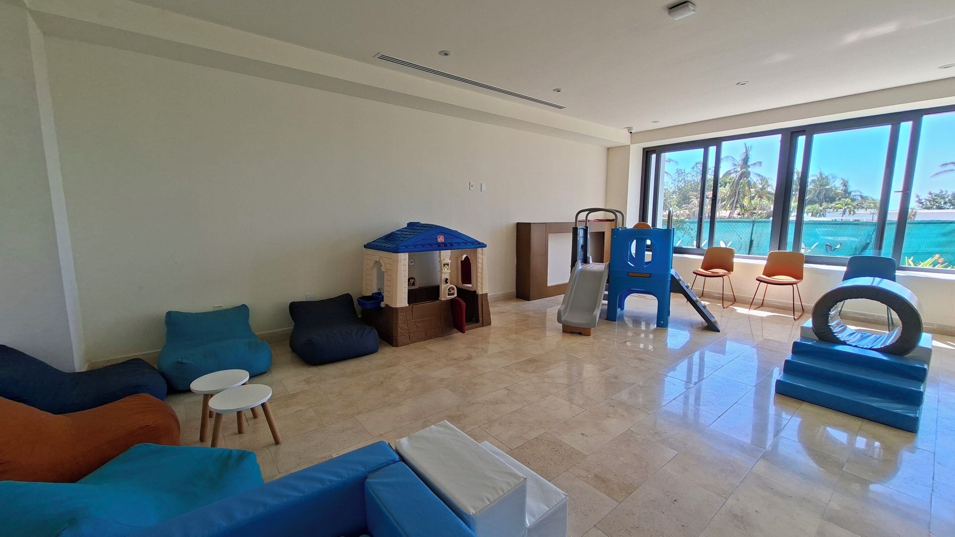 A spacious living area with a play structure, comfortable seating, and large windows offering a view of the outdoors.