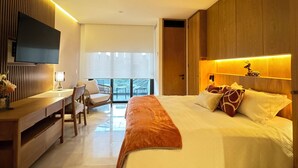 Una habitación de hotel moderna con una cama grande, un escritorio y un balcón con mobiliario exterior.