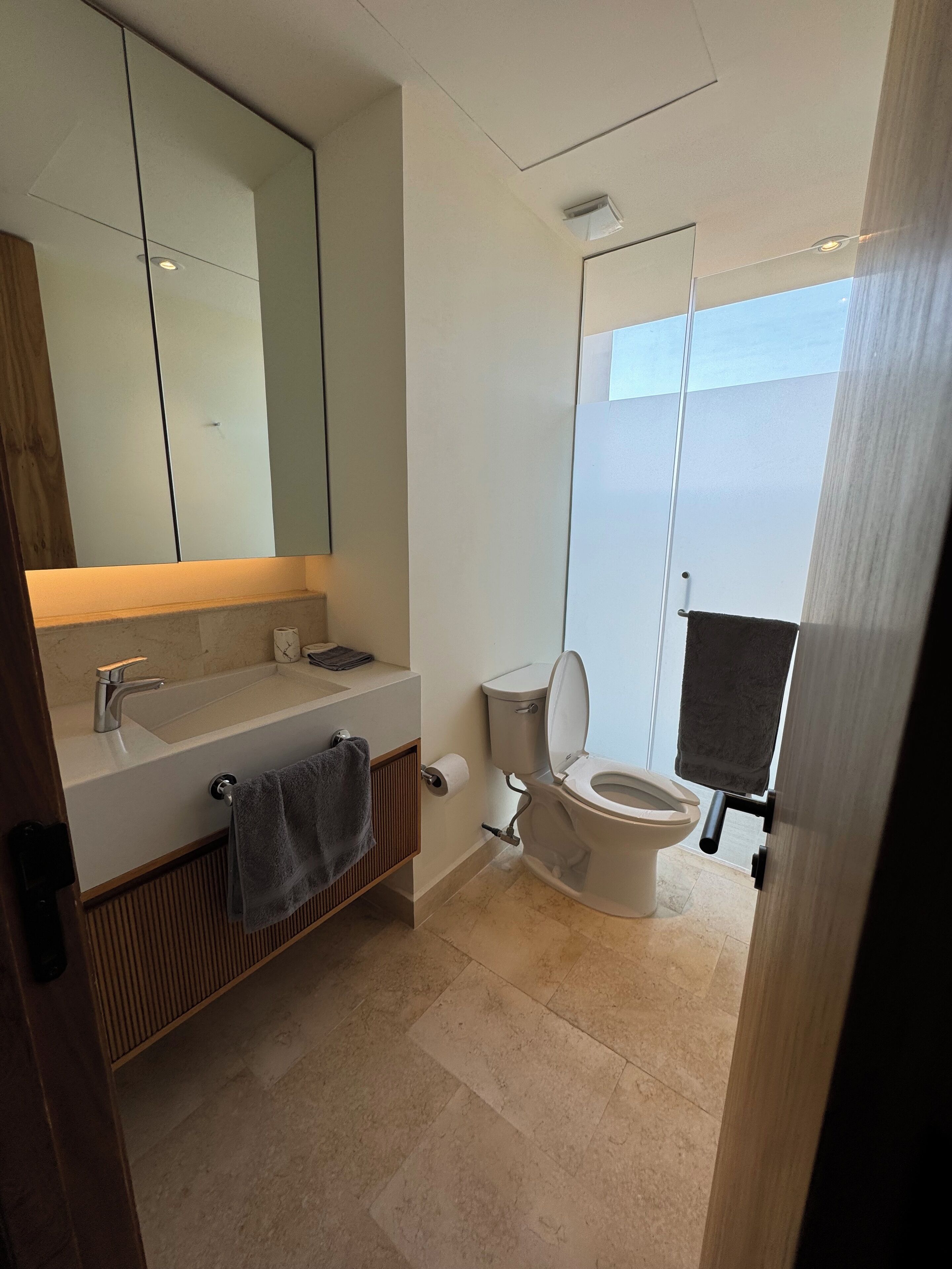 A modern bathroom with a large mirror, a sink, a toilet, and a shower enclosure.