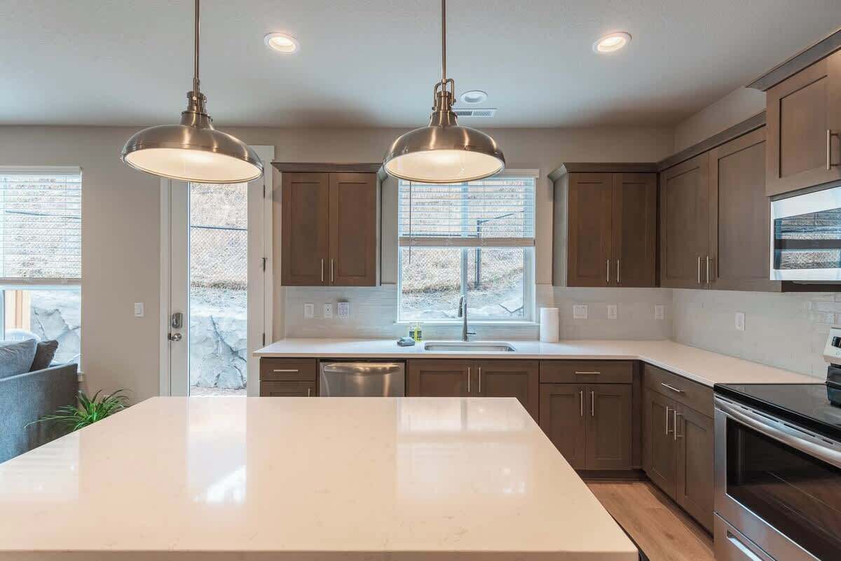 A modern kitchen with a large island, pendant lighting, and a view of the outdoors through a window.