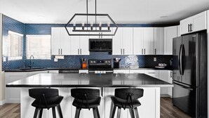 A modern kitchen with white cabinets, a black refrigerator, and a blue-tiled backsplash. - Heated Pool, Hot Tub, Game Room & Sport Court (Glendale)