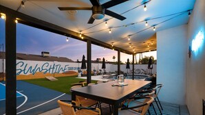 An outdoor patio area with a table and chairs, a ceiling fan, string lights, and a basketball court with a mural. - Heated Pool, Hot Tub, Game Room & Sport Court (Glendale)