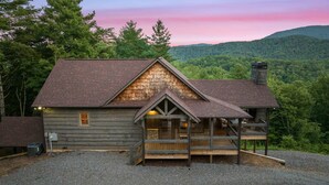 A rustic cabin with a stone chimney, wooden deck, and a view of a forested mountain range. - Surreal Views~Outdoor Fireplace Pool Table&Hot Tub (Epworth)
