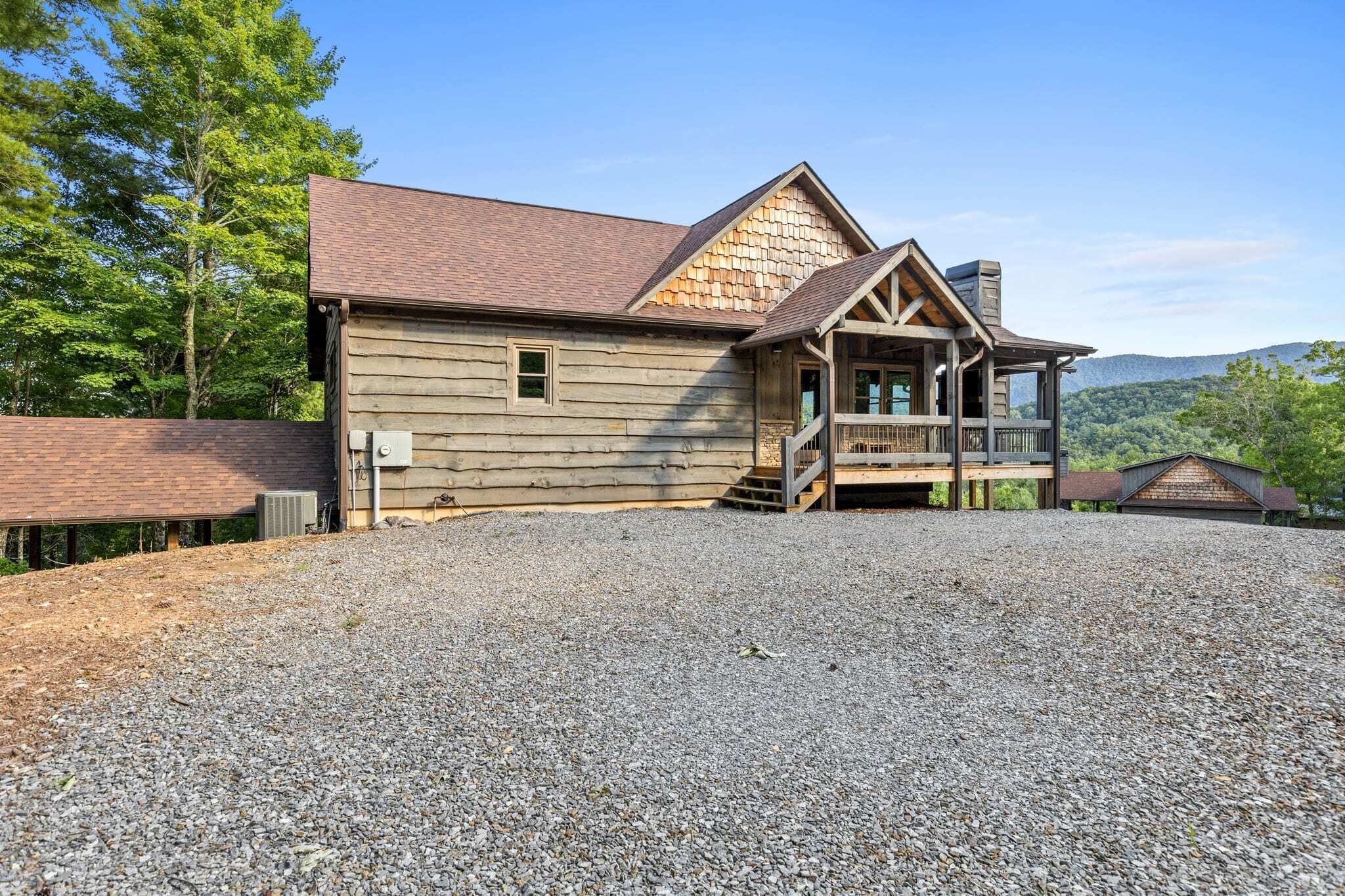 A wooden cabin with a porch, a chimney, and a gravel driveway.