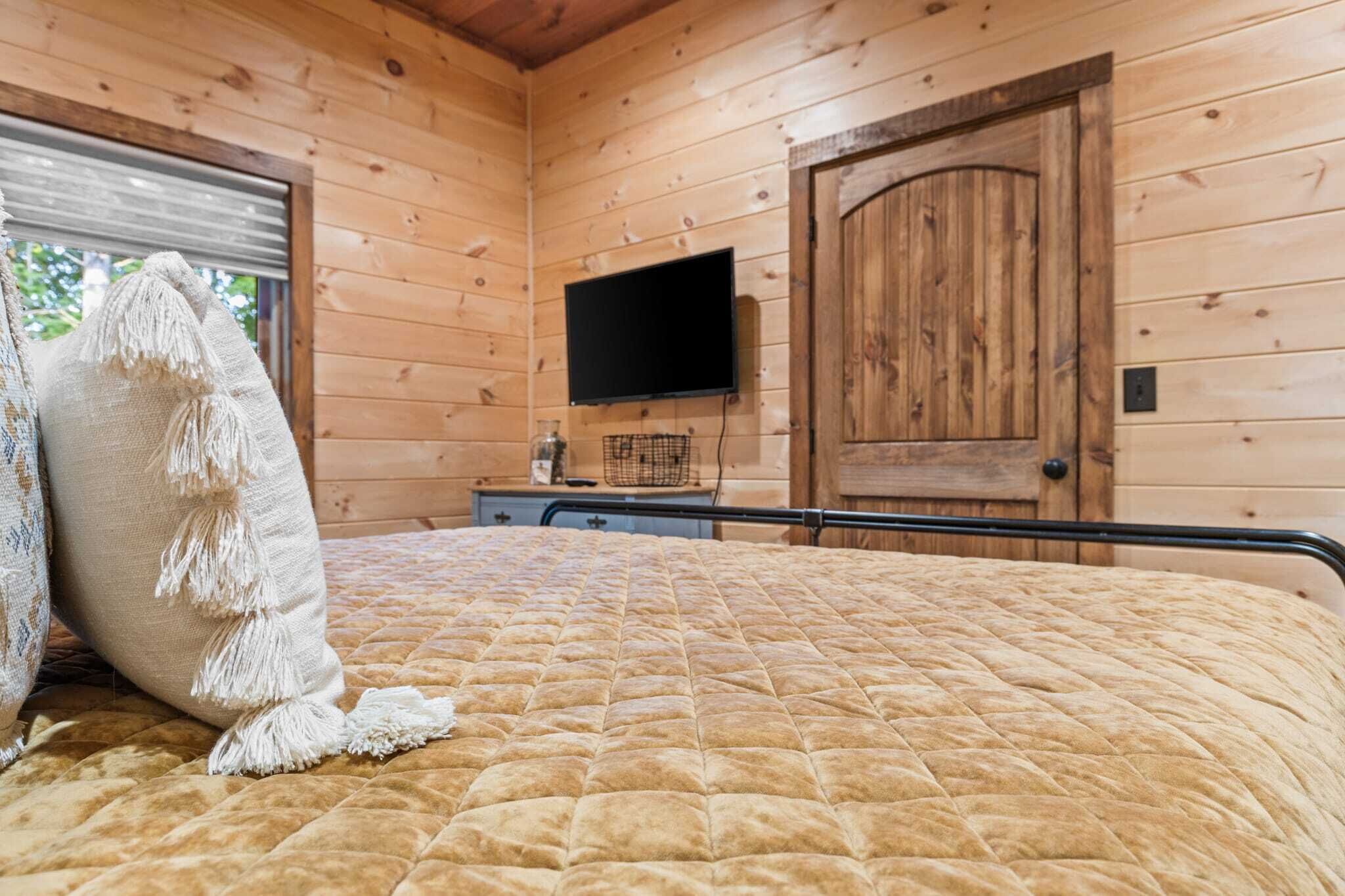 A wooden-paneled room with a bed, a television mounted on the wall, and a door.