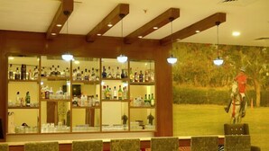 A bar area with multiple shelves of liquor bottles, a mural of a person on horseback, and several chairs. - Caelum Atharva Palace  (Jaipur)