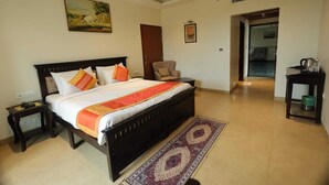 A bedroom with a large bed, a nightstand, a chair, and a small table with a kettle. - Caelum Atharva Palace  (Jaipur)