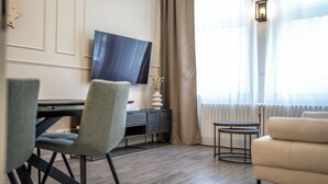 A modern living room with a flat-screen TV, a dining table, two chairs, a small side table, and a sofa. - Geli Homes L1 - 2x Kingsize Bett, 1 bis 4 Pers, Parkplatz, TV, Wifi, Kaffee, Tee (Lünen)