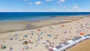A beach with numerous sunbeds and umbrellas, a sandy shore, and a clear blue sky.