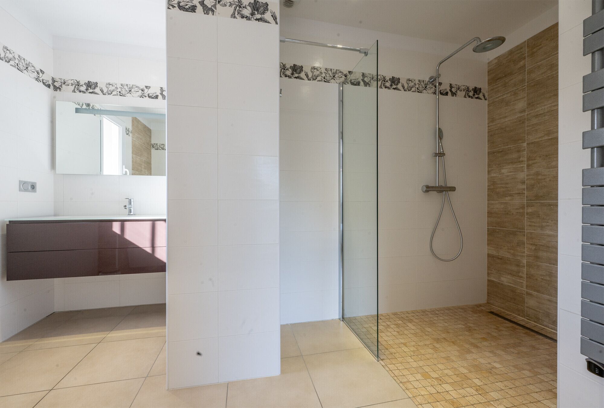 A modern bathroom with a glass shower enclosure, a wooden vanity, and a tiled floor.