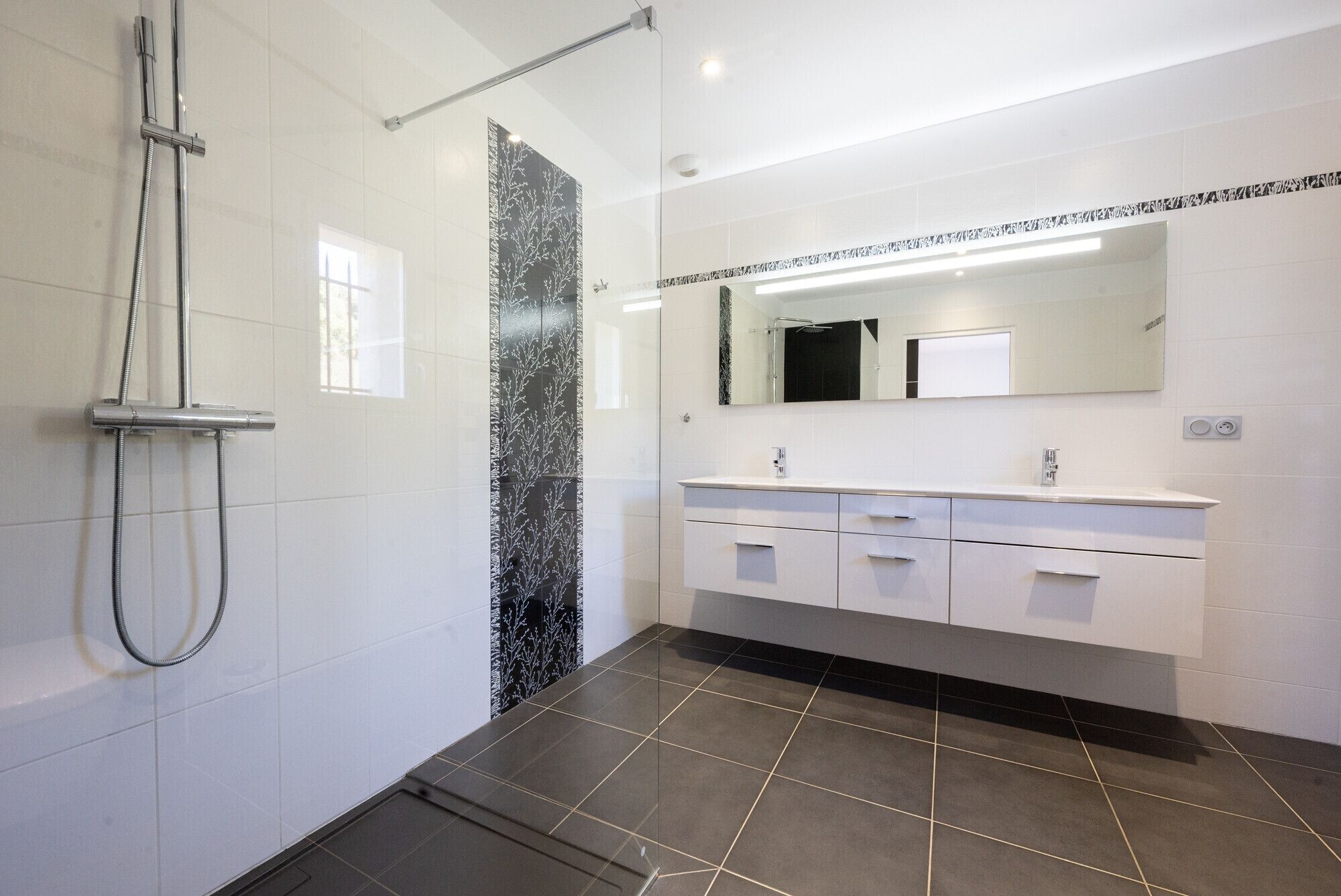 A modern bathroom with a shower, a large mirror, and a vanity with drawers.