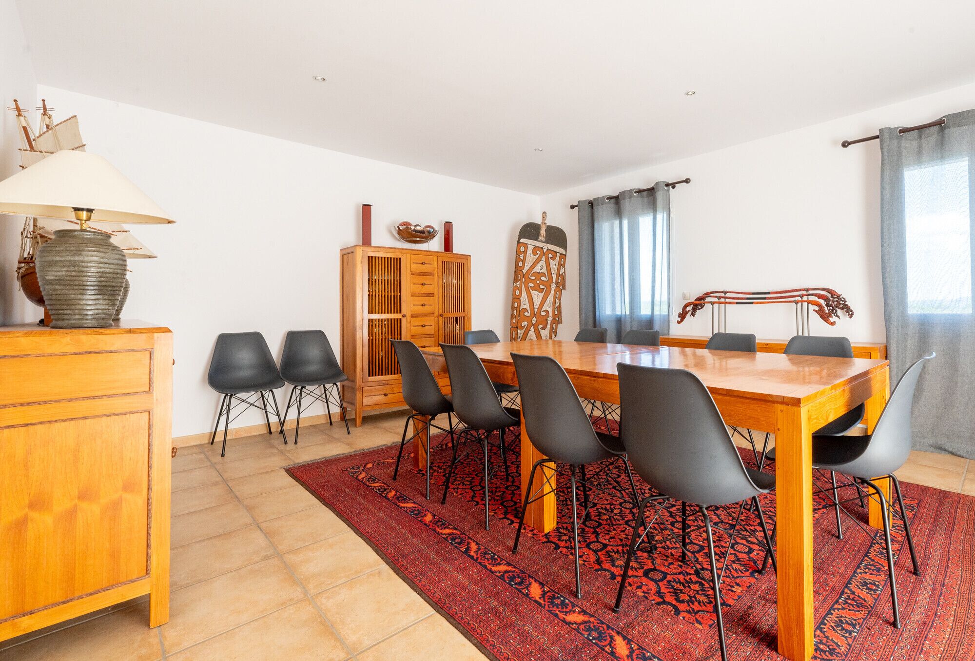 Un coin repas avec une table en bois, des chaises noires, un tapis rouge à motifs, un meuble en bois et une lampe en forme de bateau.