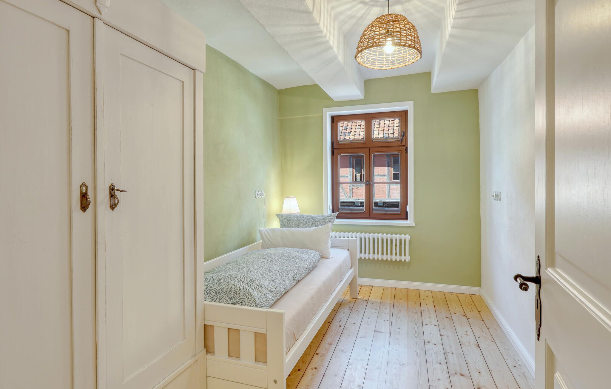 A small, well-lit room with a single bed, a window with a view of buildings, and a radiator under the window.