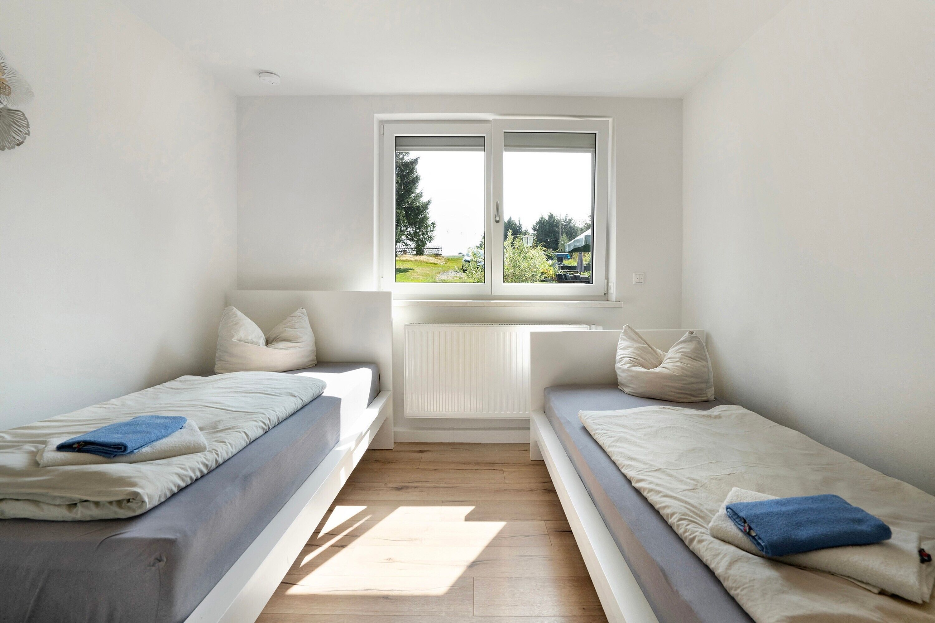 A small, bright room with two beds, a window with a view, and a radiator.