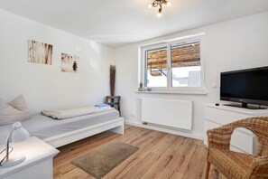 Une chambre à coucher comprenant un lit, une table de chevet, une lampe, un téléviseur et une fenêtre avec des stores.