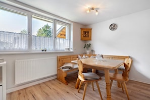 Un coin repas avec une table et des chaises en bois, un radiateur, une fenêtre avec des rideaux et une horloge au mur.