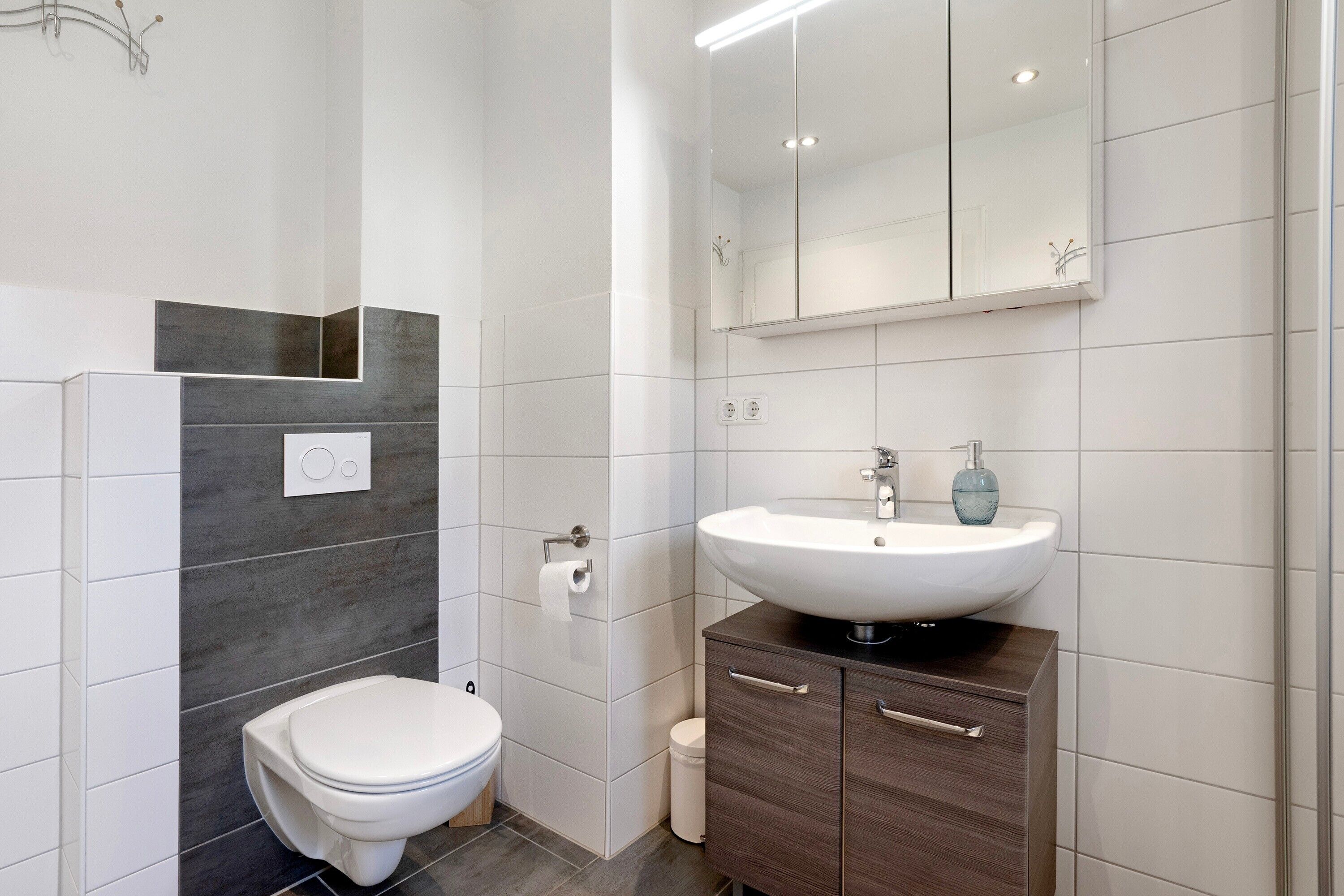 A modern bathroom with a toilet, a sink, a mirror, and a cabinet.