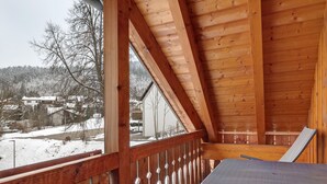 Un balcon en bois offrant une vue sur un paysage enneigé et sur des maisons.
