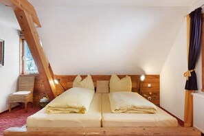 Une pièce avec un plafond en pente, des poutres en bois, un lit avec deux oreillers, une chaise, une petite table et une fenêtre.