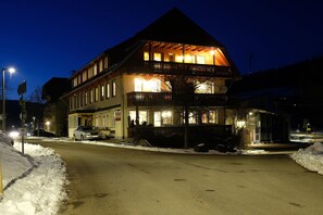 Un edificio di due piani con un balcone, un cartello con la scritta 'Krone' e una strada coperta di neve.
