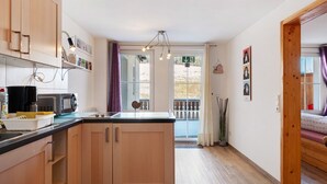 Una cocina con armarios de madera, un microondas y un lavamanos. Se ve una ventana con cortinas y vistas al exterior.