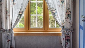 A bedroom with a wooden window sill, floral curtains, and a checkered bedspread.