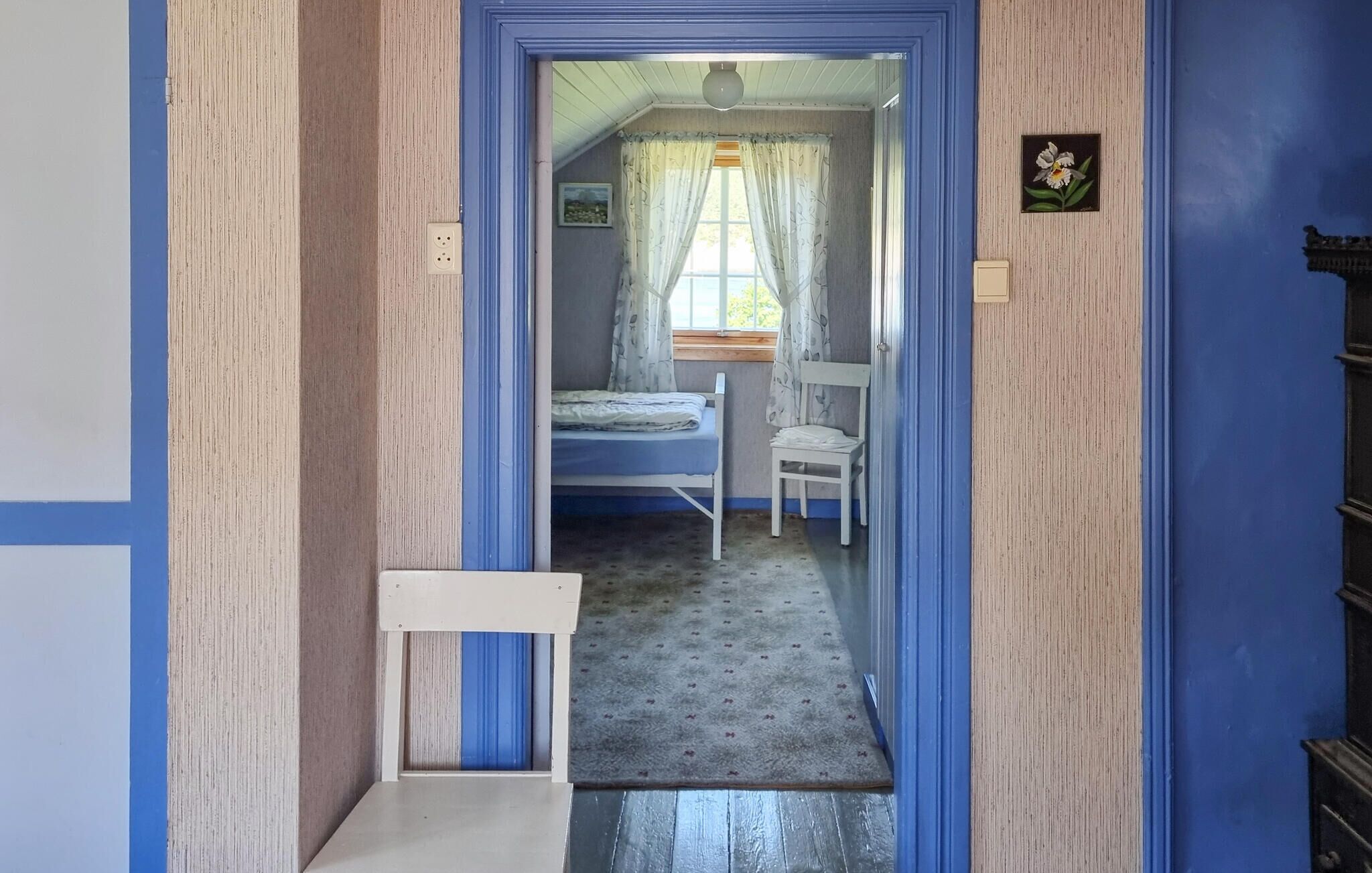 Ein schmaler Flur führt zu einem Schlafzimmer mit Bett, Stuhl und einem kleinen Tisch.
