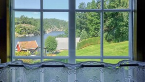 A window with a view of a lake, a red building, and green trees.