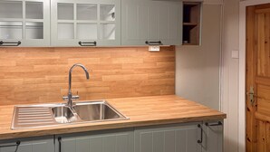 A kitchen with a stainless steel sink, wooden countertop, and light grey cabinets.