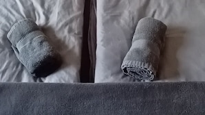 Un lit avec une literie et des oreillers gris, une couverture grise et un coussin gris posé sur la tête de lit.