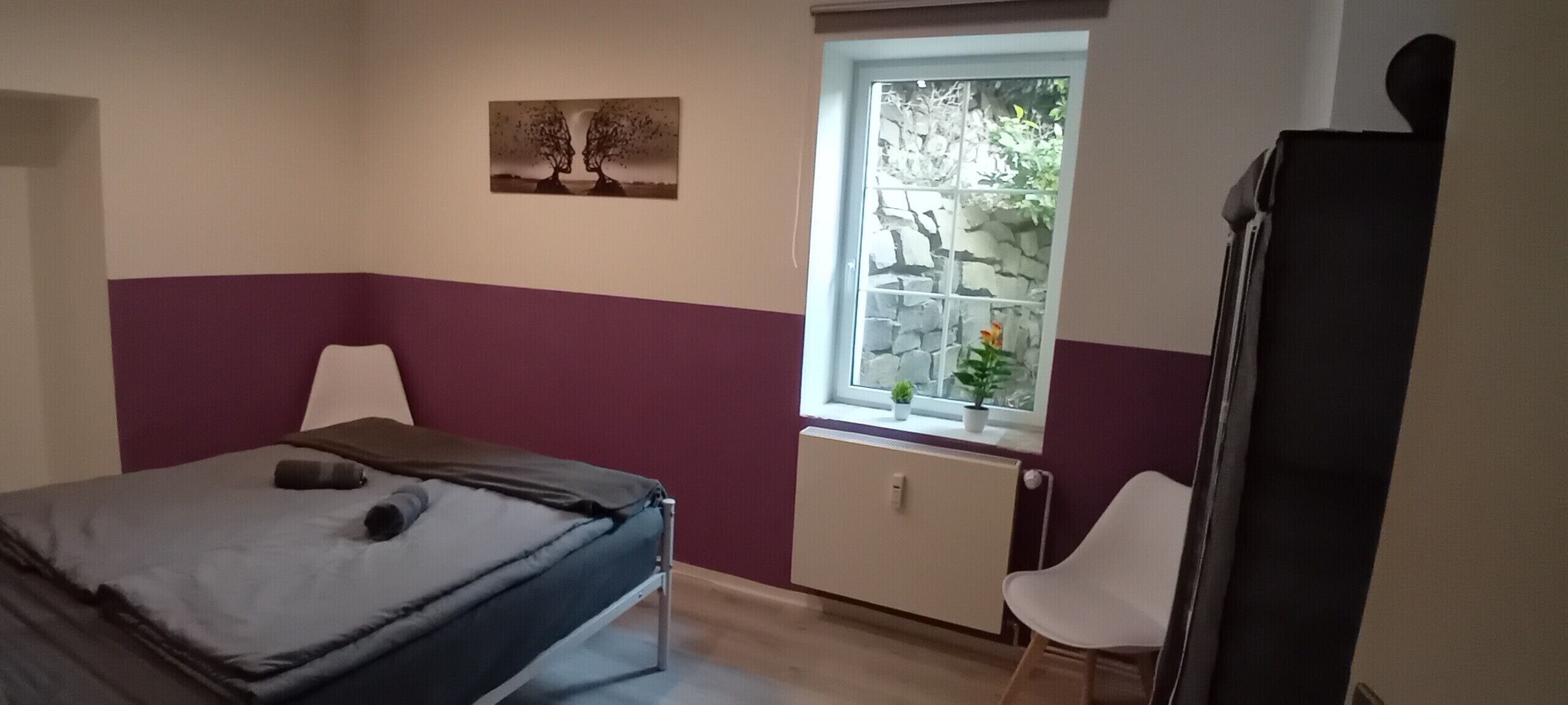 Een slaapkamer met een bed, een raam met uitzicht, een radiator en een stoel.