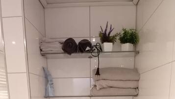 A bathroom with a toilet, a towel rack, and a shelf with plants.