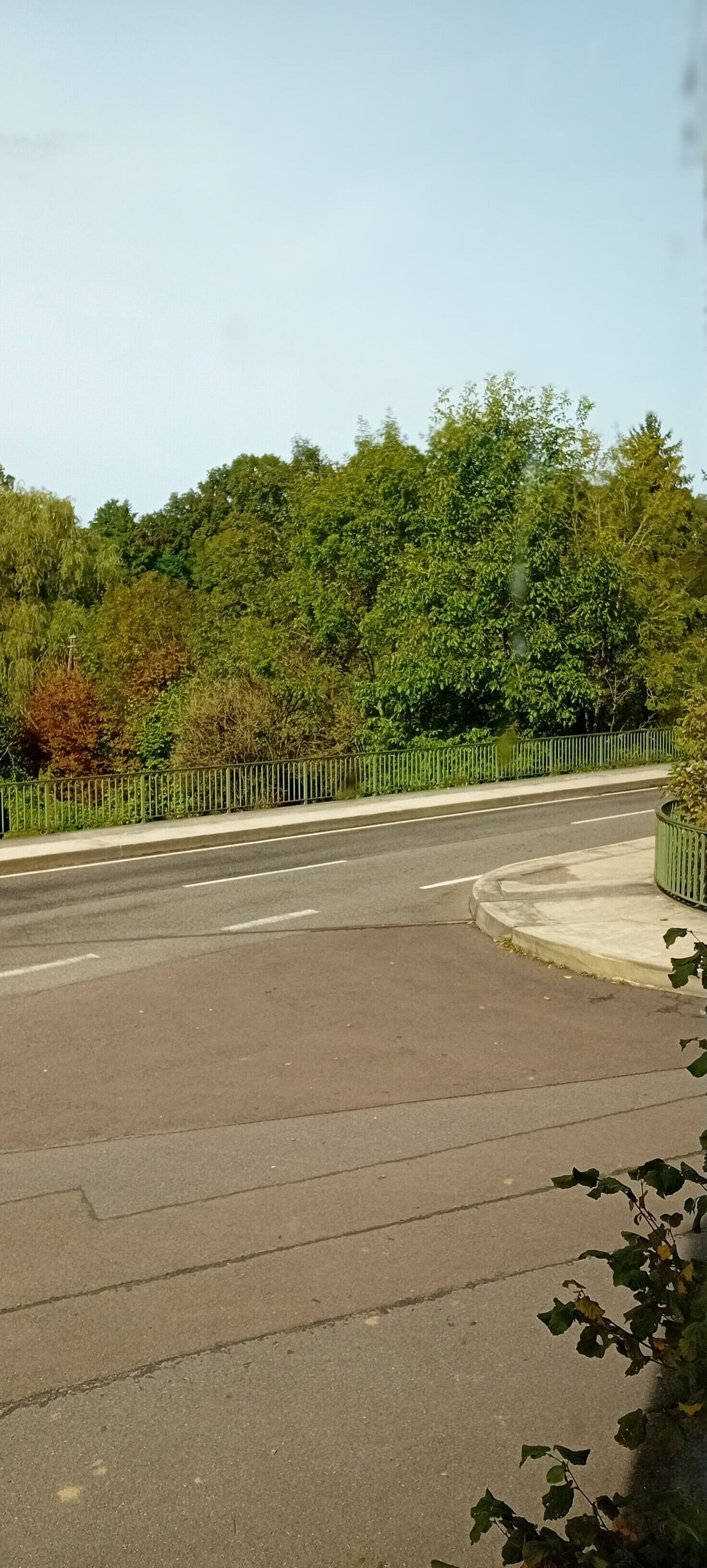 A road with a sidewalk and a green fence.