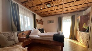 A cozy room with a wooden ceiling, a bed with white bedding, a wooden dresser, and a fluffy white rug.