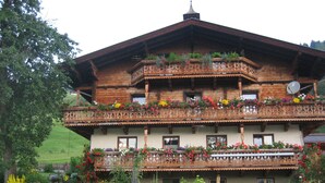 A multi-story wooden building with balconies adorned with flowers, surrounded by a well-maintained garden.