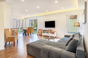 A spacious living area with a grey sofa, a dining table with chairs, a flat-screen TV mounted on the wall, and a lamp on a side table. - Apartment 'Ferienwohnung Auszeit' with Private Terrace, Private Garden and Wi-Fi (Solnhofen)