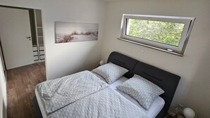 Een slaapkamer met een bed, een raam, een deur en een aan de muur hangend schilderij.