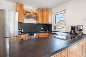 A modern kitchen with a stainless steel refrigerator, a built-in oven, a coffee machine, and wooden cabinets. - Apartment 'Ferienwohnung Auszeit' with Private Terrace, Private Garden and Wi-Fi (Solnhofen)