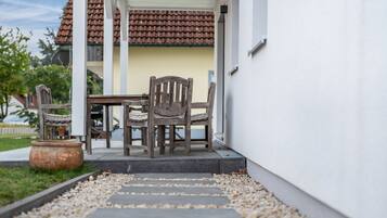Um pátio com mesa e cadeiras, um vaso de planta e um caminho que leva a um edifício com telhado telhado.