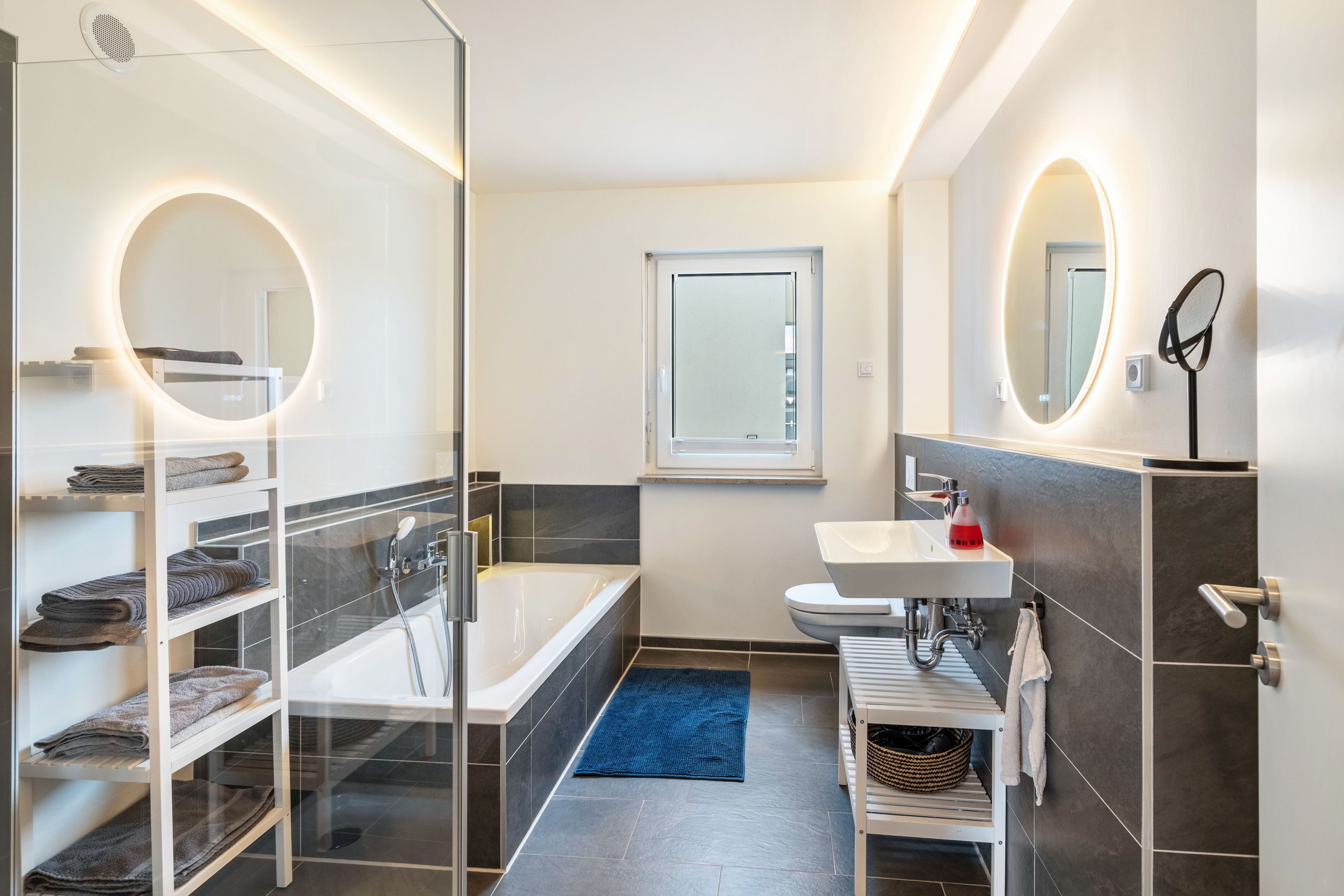 Ein modernes Badezimmer mit einer Duschkabine aus Glas, einem weißen Waschbecken und einem großen Spiegel.