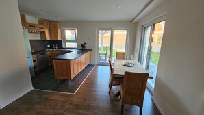 Een moderne keuken met een centraal eiland, houten keukenkastjes en een eethoek met een tafel en stoelen.