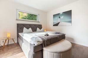 Une chambre à coucher avec un lit, une fenêtre, une table de chevet, une lampe et un tableau au mur.