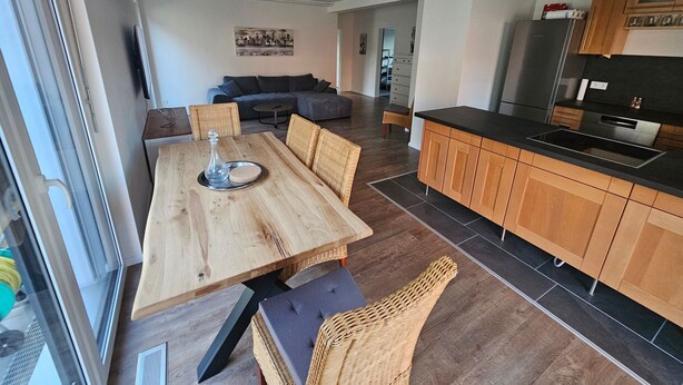 Een moderne keuken met houten kastjes, een eettafel met stoelen, en een zithoek met een bank en salontafel.
