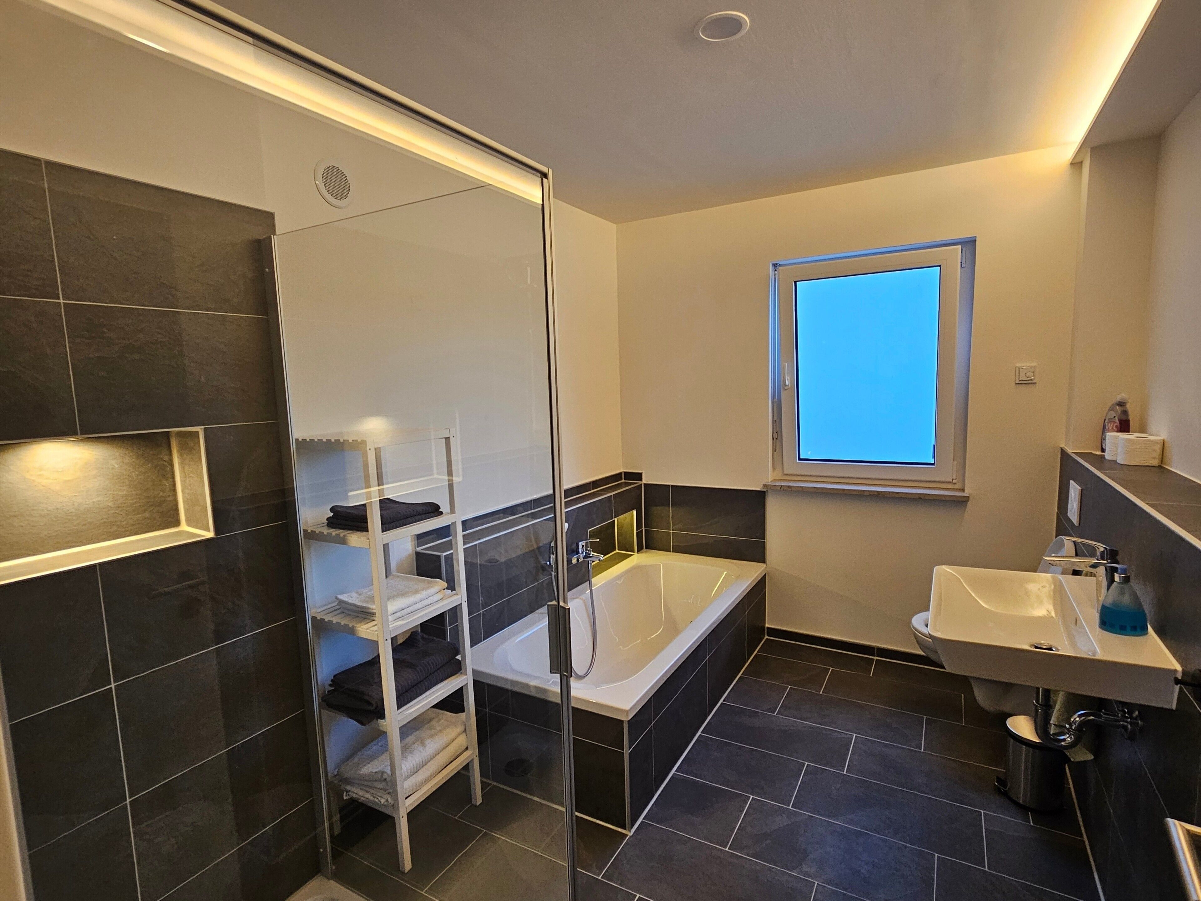Een moderne badkamer met een douchecabine van glas, een vrijstaand bad, een wastafel en een raam voor natuurlijk licht.