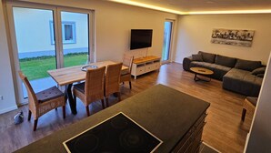 Een moderne woonruimte met een eethoek, een flatscreen-tv, een bank en een keuken met fornuis.