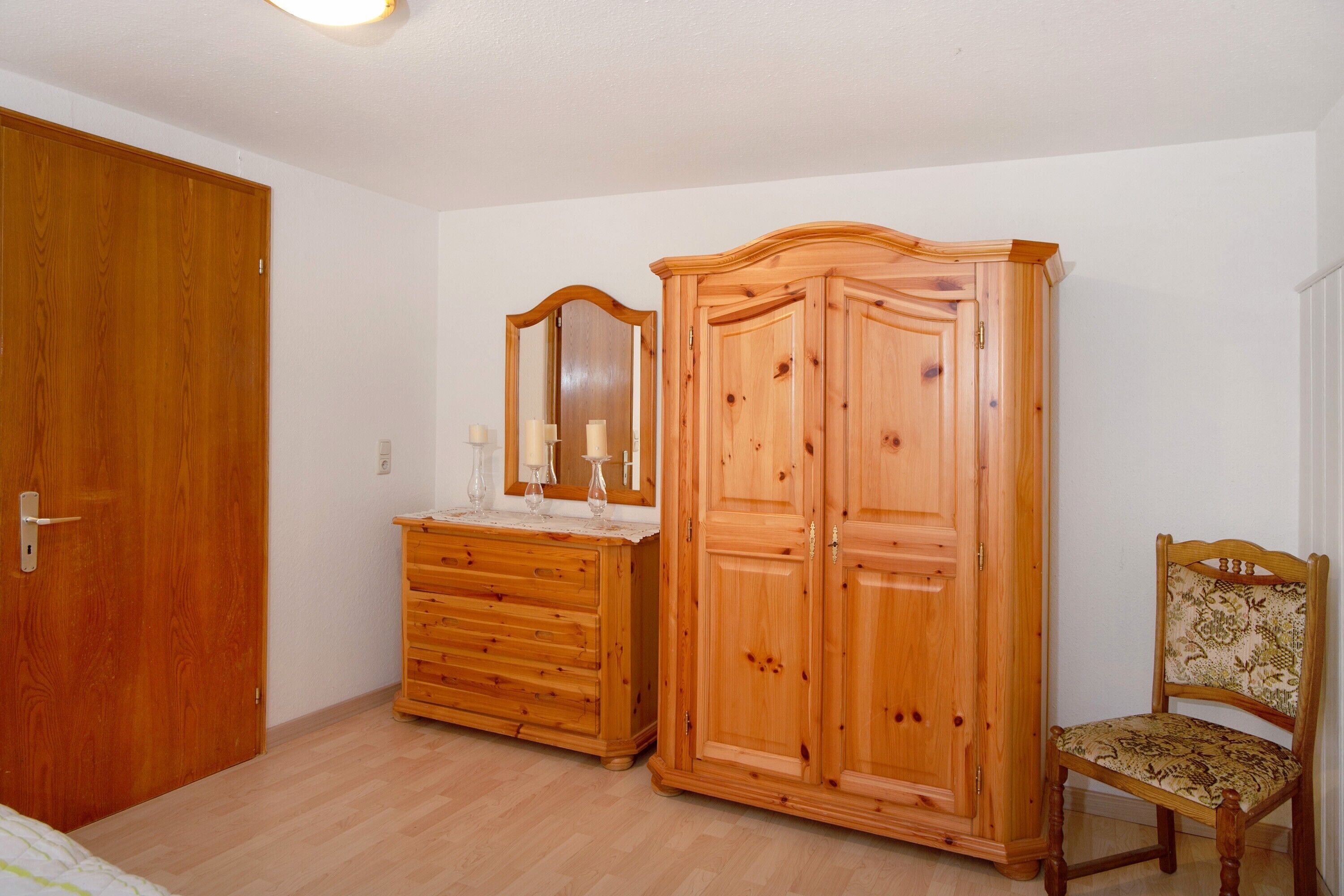 Ein Schlafzimmer mit Holzmöbeln, darunter ein Kleiderschrank, eine Kommode und ein Stuhl.